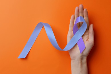 Image of World Arthritis Day. Woman with blue and purple awareness ribbon on orange background, top view