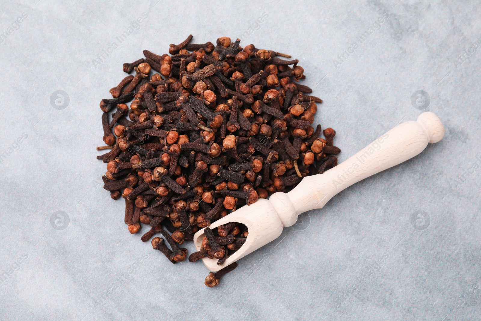 Photo of Pile of aromatic dried clove buds and scoop on grey table, top view