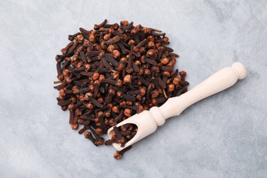 Pile of aromatic dried clove buds and scoop on grey table, top view