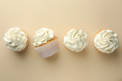 Photo of Tasty vanilla cupcakes with cream on beige background, top view