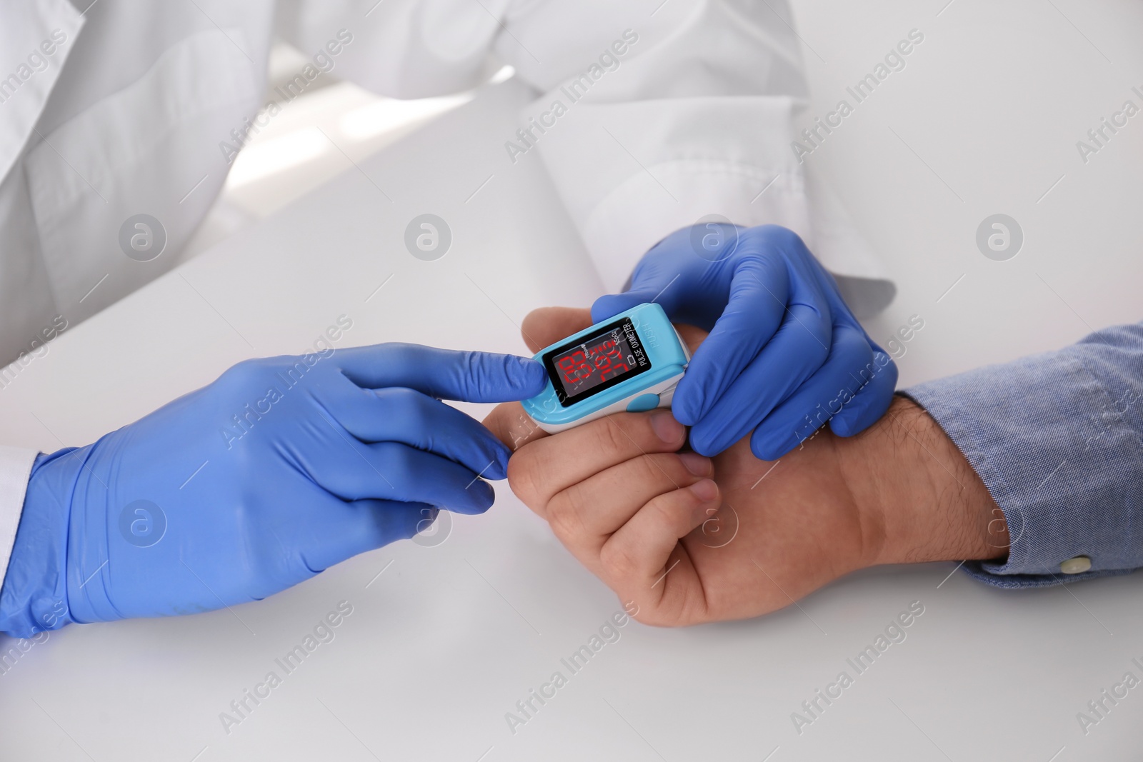 Photo of Doctor checking patient's oxygen level with pulse oximeter at light grey table, closeup