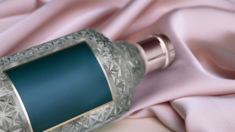 Bottle of luxurious perfume on beige silk, closeup