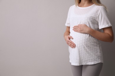 Pregnant woman on light grey background, closeup. Space for text