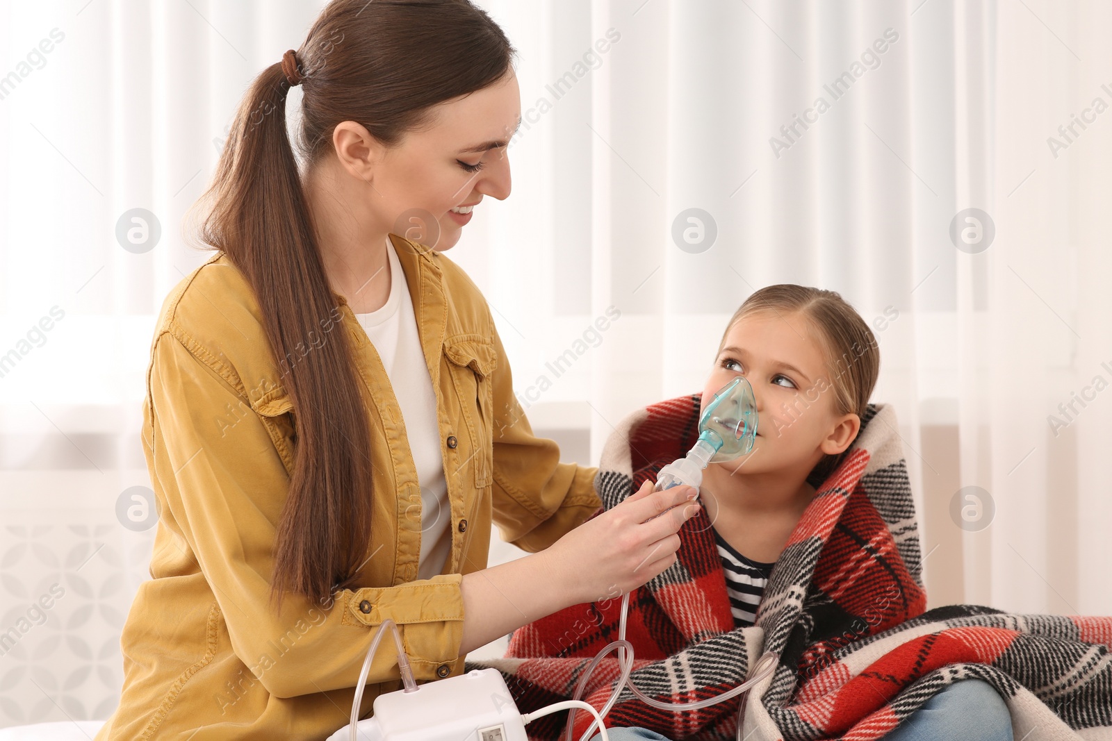 Photo of Mother helping her sick daughter with nebulizer inhalation at home