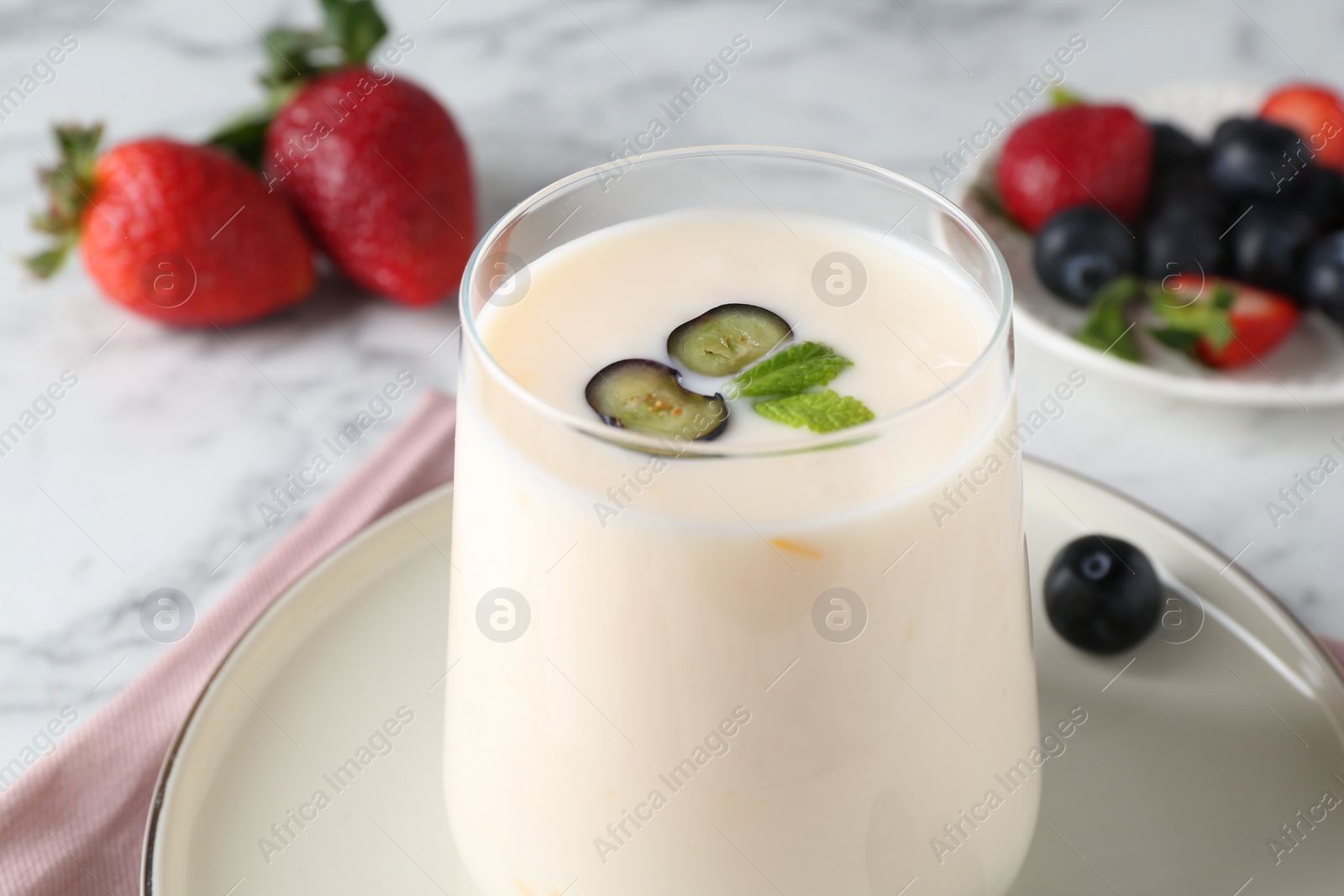 Photo of Tasty yogurt in glass and berries on white table, closeup