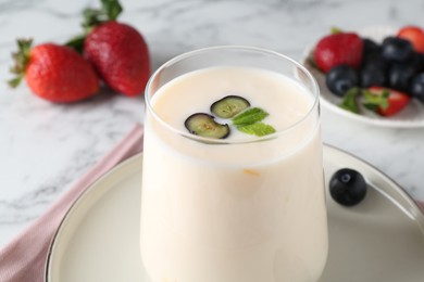 Photo of Tasty yogurt in glass and berries on white table, closeup