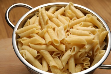 Cooked pasta in metal colander on wooden table, closeup