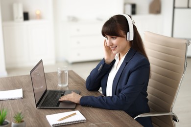 Woman in headphones watching webinar at wooden table in office