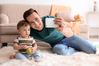 Photo of Young father with his cute little son taking selfie at home