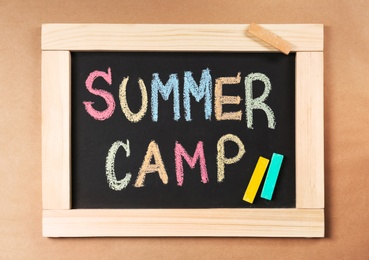 Photo of Words SUMMER CAMP written with colorful chalk on small blackboard, top view