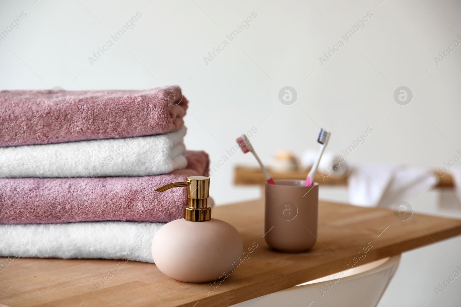 Photo of Stack of clean soft towels, soap dispenser and toothbrushes in bathroom