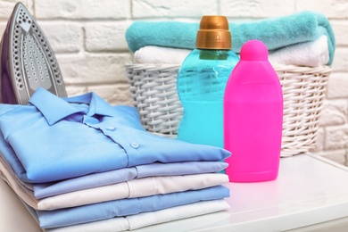 Photo of Stack of clean clothes, iron, detergents and basket with towels on table