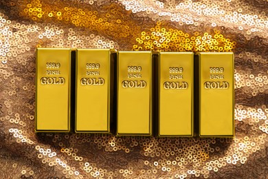 Photo of Many shiny gold bars on bronze sequin fabric, flat lay