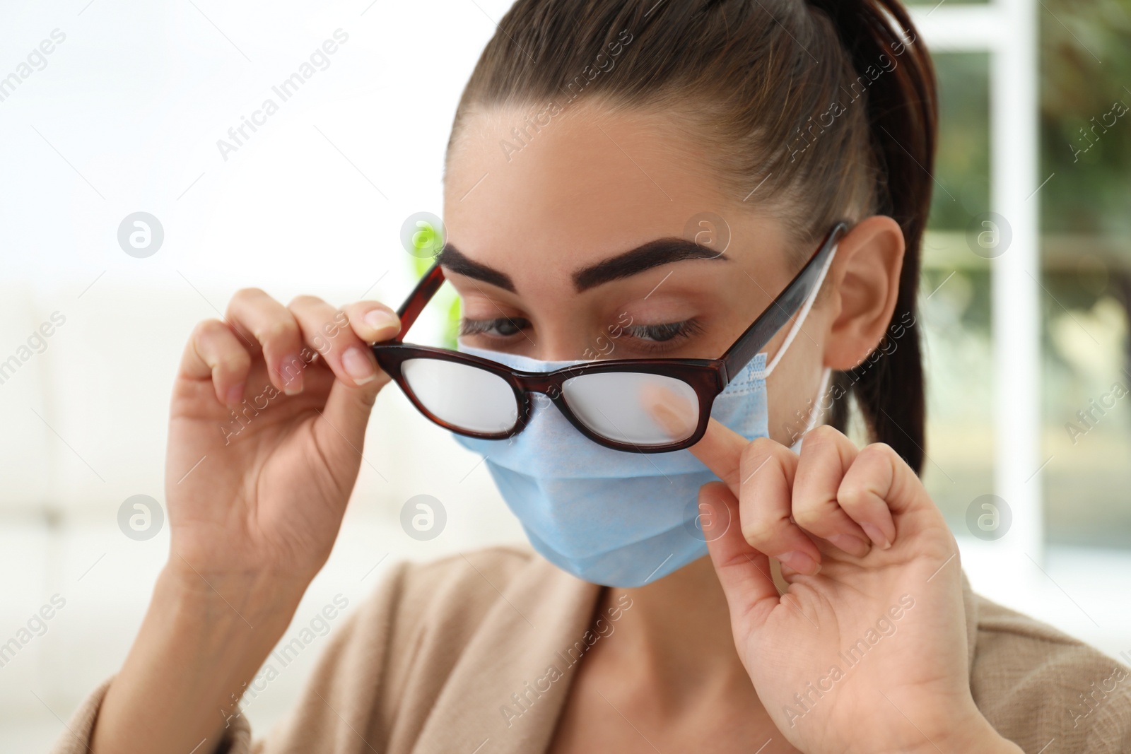 Photo of Woman wiping foggy glasses caused by wearing medical mask indoors, closeup