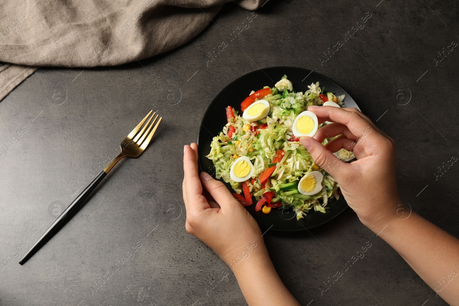 Photo of Woman making delicious salad with Chinese cabbage and quail eggs at black table, top view