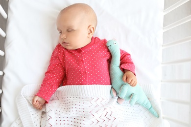 Cute baby girl sleeping in crib, top view