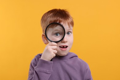 Surprised boy looking through magnifier glass on yellow background