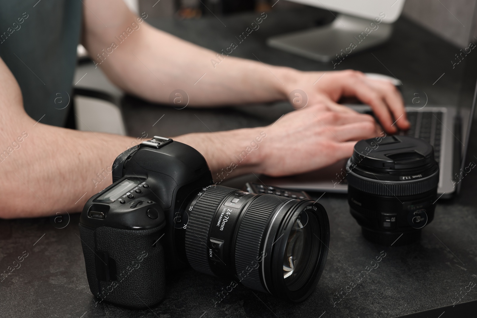 Photo of Camera on dark table, closeup. Photographer working with computer indoors, selective focus