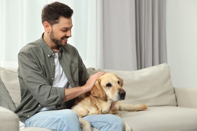 Happy man sitting on sofa with his cute Labrador Retriever at home. Space for text