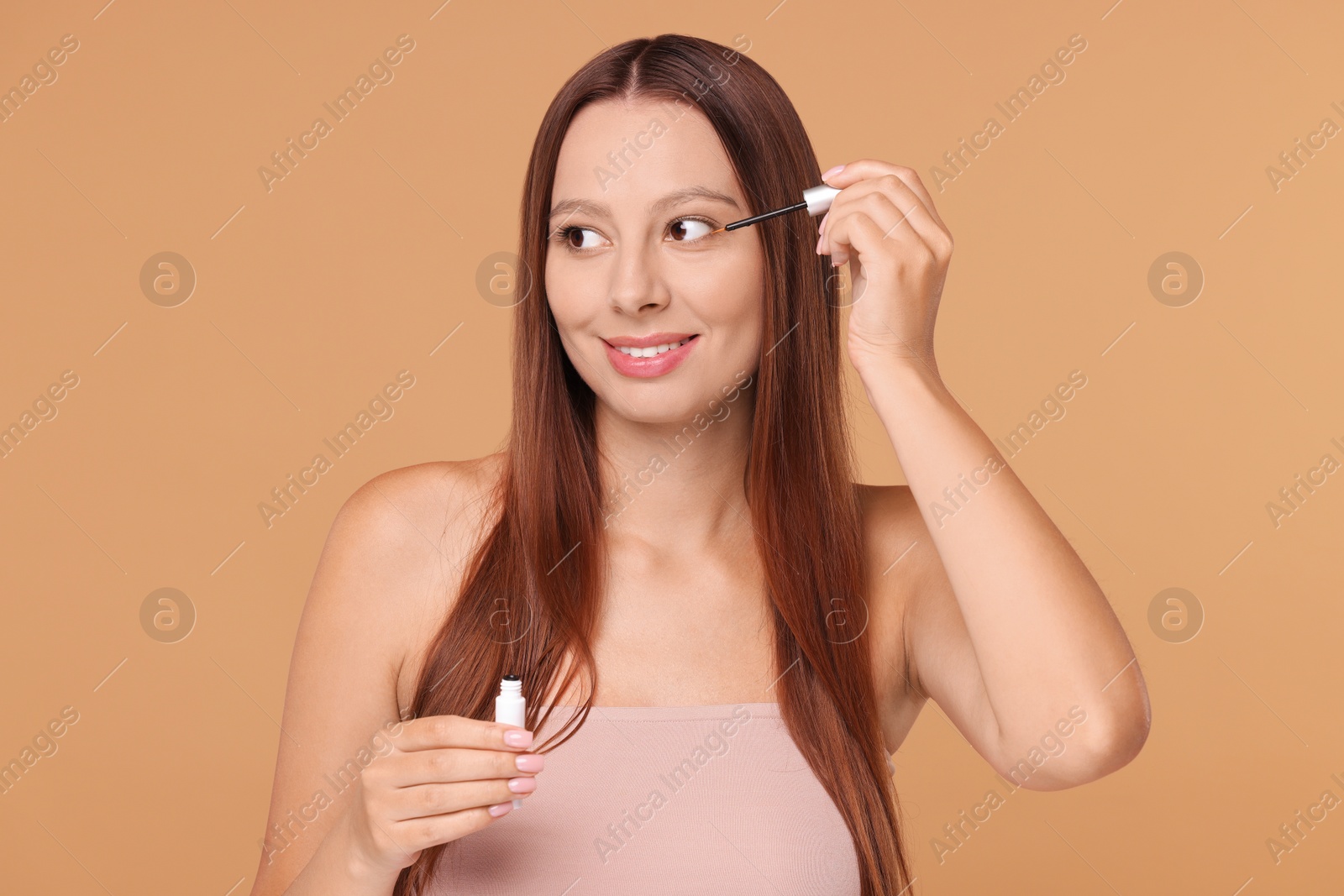 Photo of Beautiful woman applying serum onto eyelashes on beige background