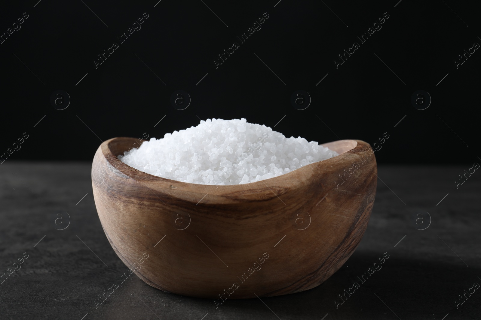 Photo of Natural salt in wooden bowl on dark grey table