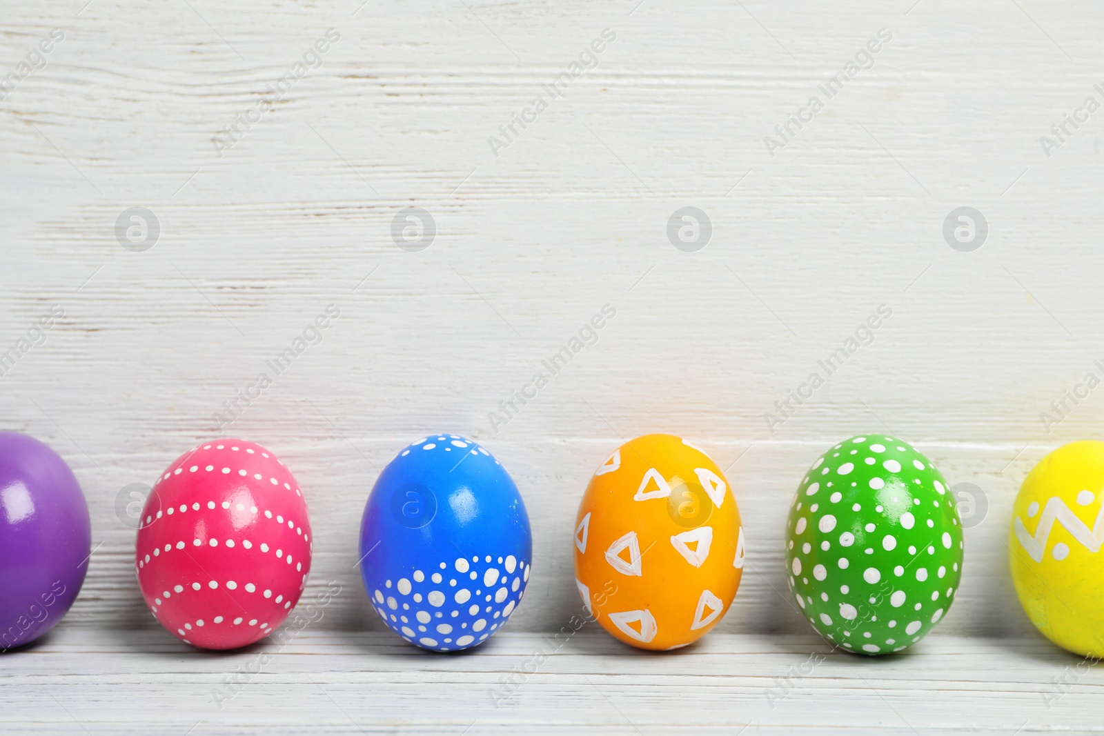 Photo of Decorated Easter eggs on table near wooden wall. Space for text