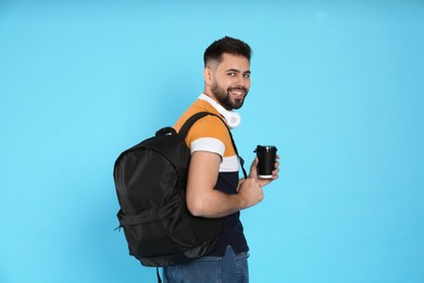 Photo of Young man with stylish backpack, headphones and cup of coffee on light blue background