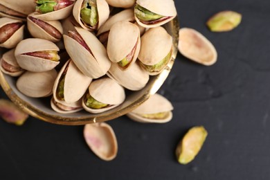 Photo of Tasty pistachios in bowl on black table, closeup. Space for text