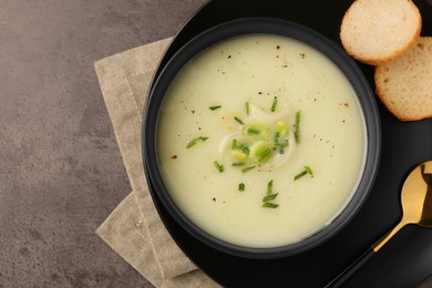 Photo of Bowl of tasty leek soup, spoon and bread on grey table, flat lay. Space for text