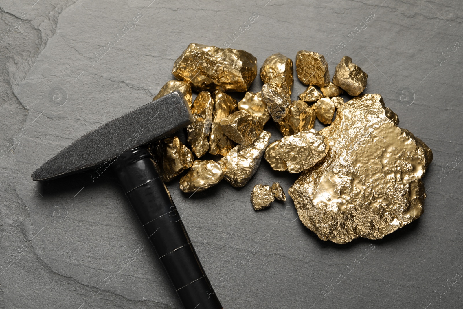 Photo of Pile of gold nuggets and hammer on black table, flat lay