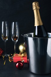 Photo of Happy New Year! Bottle of sparkling wine in bucket and glasses on black background