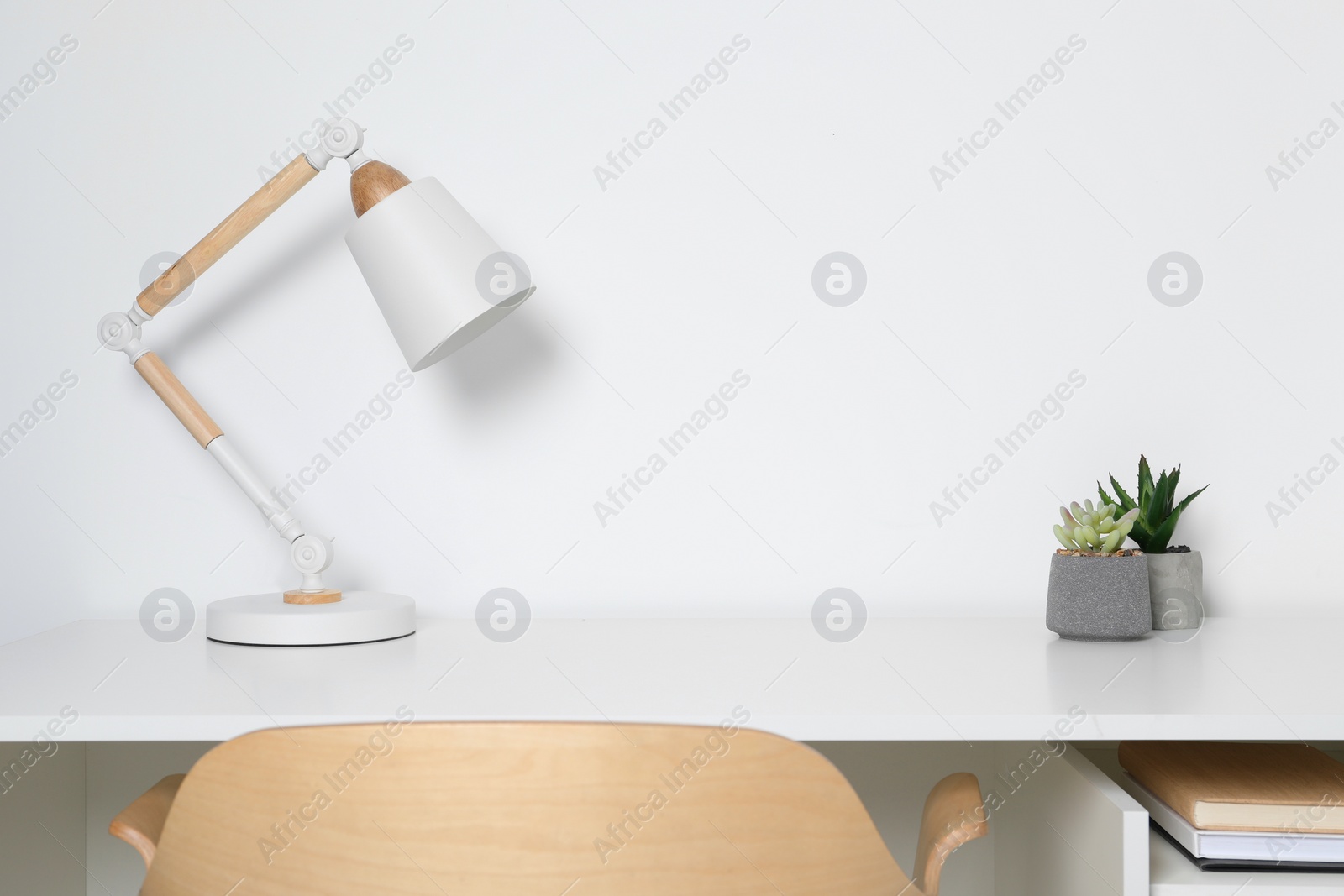 Photo of Stylish modern desk lamp and potted succulents on table near white wall indoors