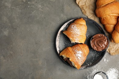 Flat lay composition with tasty croissants, chocolate paste and sugar powder on grey table. Space for text