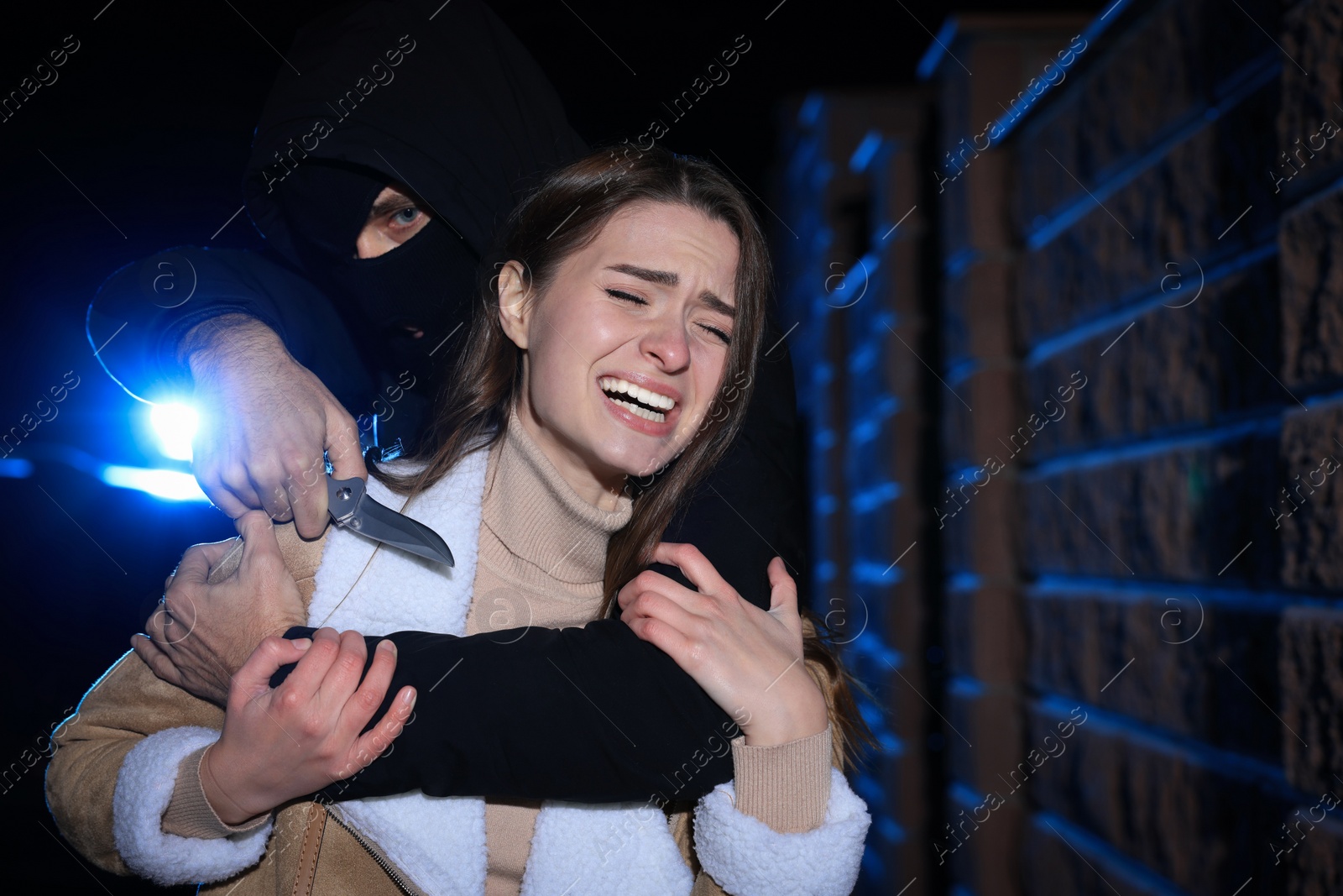 Photo of Criminal with knife attacking young woman outdoors at night. Self defense concept