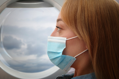 Traveling by airplane during coronavirus pandemic. Woman with face mask near porthole