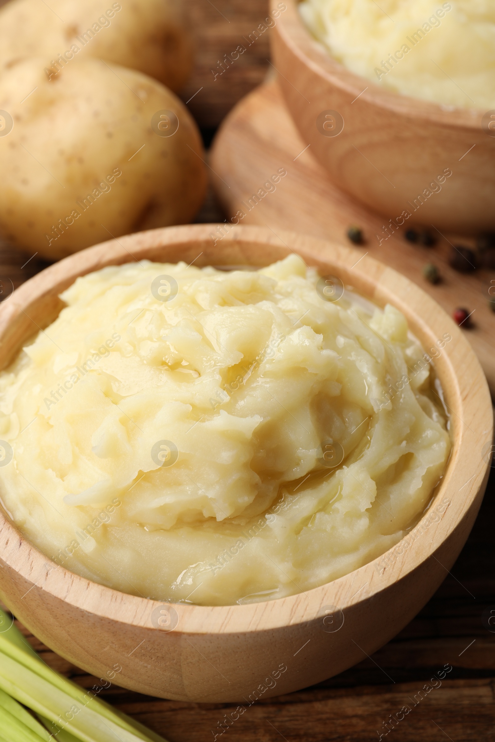 Photo of Bowls of tasty mashed potato, pepper and leeks on wooden table, closeup