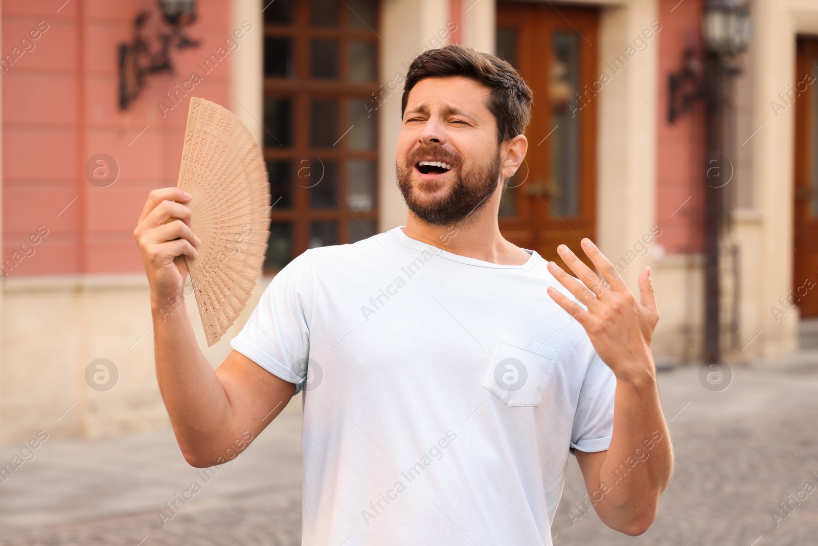 Photo of Man with hand fan suffering from heat outdoors