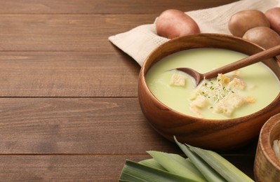 Photo of Bowl of tasty leek soup, spoon and ingredients on wooden table. Space for text