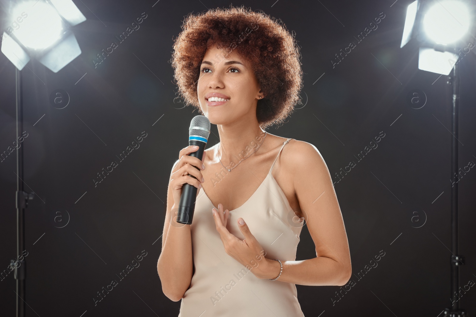 Photo of Curly young woman with microphone singing on black background