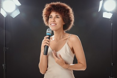Curly young woman with microphone singing on black background