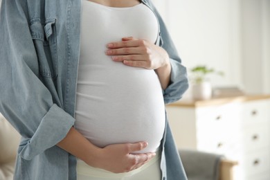 Pregnant woman touching her belly indoors, closeup