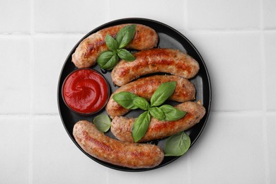 Photo of Plate with tasty homemade sausages, ketchup and basil leaves on white tiled table, top view