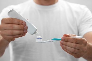 Man applying toothpaste on brush against grey background, closeup