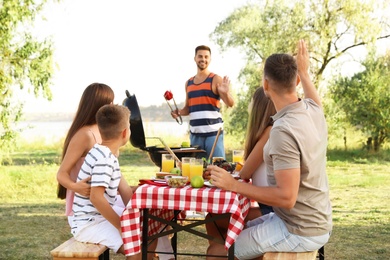 Happy young people and little boy having picnic at table in park