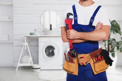 Plumber with pipe wrench and tool belt in bathroom, closeup. Space for text