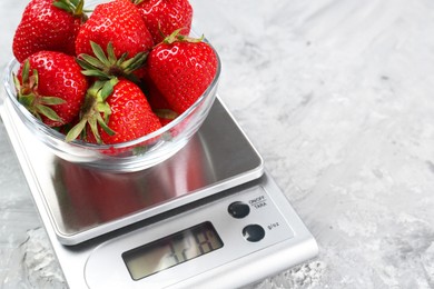 Kitchen scale with bowl of strawberries on grey textured table, closeup. Space for text