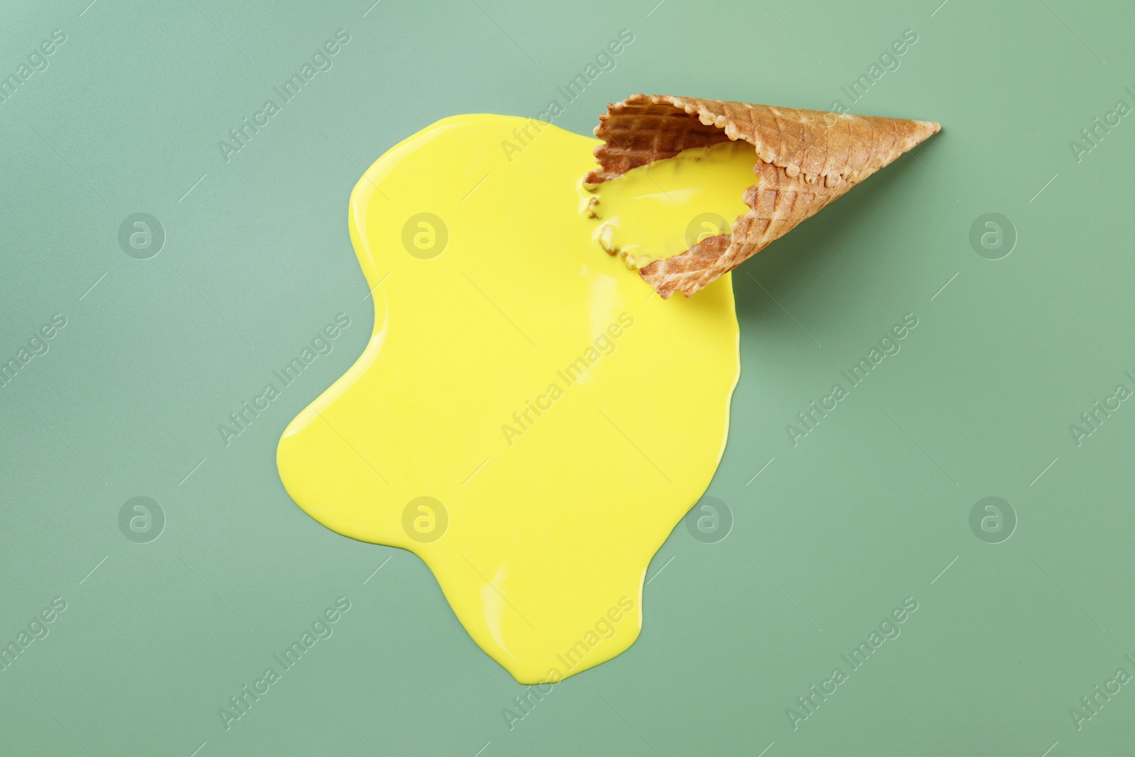 Photo of Melted ice cream and wafer cone on green background, above view