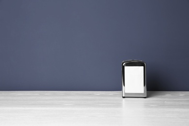 Photo of Napkin holder with paper serviettes on table against color background. Space for text