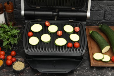 Electric grill with vegetables and spices on black marble table