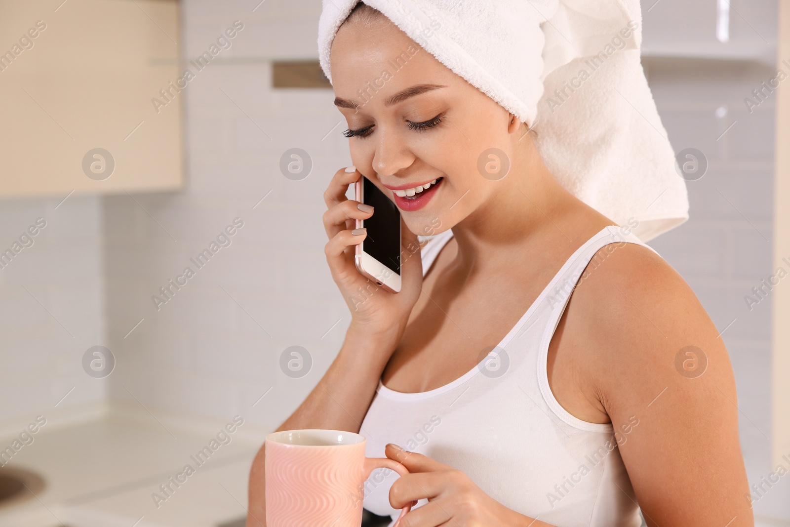 Photo of Beautiful woman with head wrapped in towel drinking tea and talking on phone at home